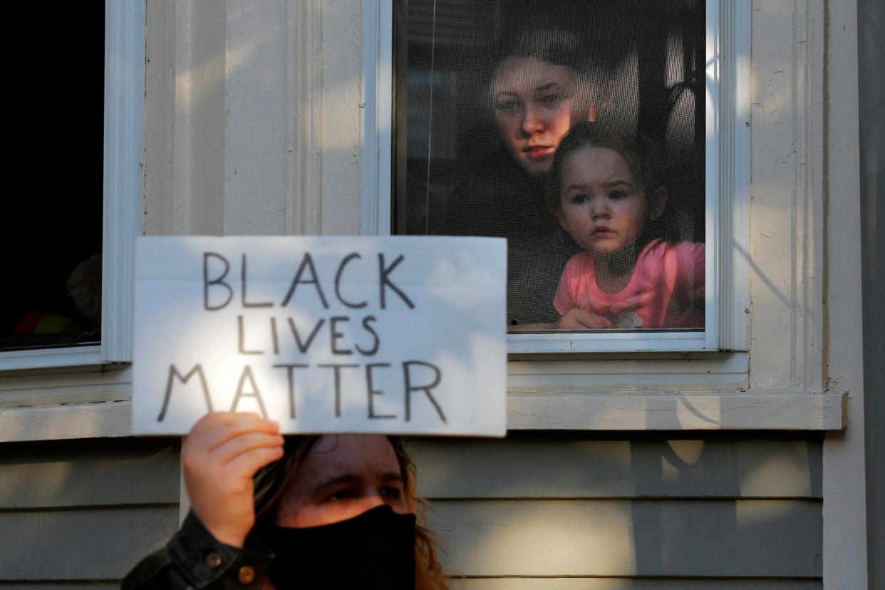 A woman and a girl watch from window as demonstrators pass by protesting against racial inequality in the aftermath of the death in Minneapolis police custody of George Floyd in Salem, Massachusetts, U.S., June 12, 2020.   (Brian Snyder/Reuters)