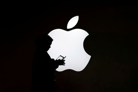 A woman looks at the screen of her mobile phone in front of an Apple logo outside its store in Shanghai, China July 30, 2017. REUTERS/Aly Song/Files