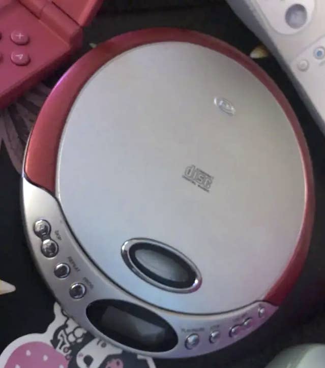 Portable CD player with circular design and external buttons on a table with gaming items