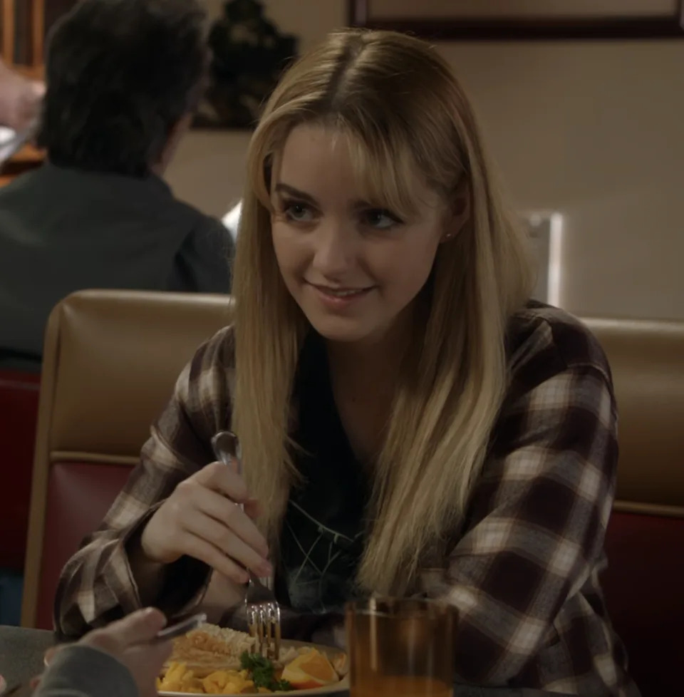 Paige in plaid shirt sits at restaurant table, wearing plaid shirt