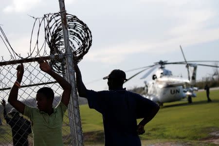 Men stand by a fence next to a United Nations helicopter at the airport after Hurricane Matthew passes Jeremie, Haiti, October 7, 2016. REUTERS/Carlos Garcia Rawlins