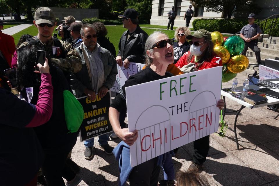 Small crowd stands on a lawn, some holding signs like 'Free the Children'