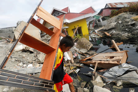 A boy carries a piece of wooden furniture in the earthquake and liquefaction affected Balaroa neighbourhood in Palu, Central Sulawesi, Indonesia, October 11, 2018. REUTERS/Darren Whiteside