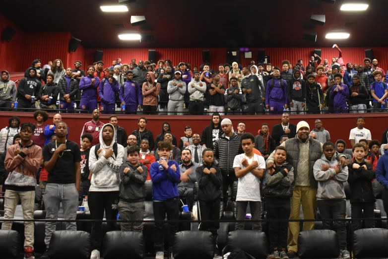 Students make the Wakanda Forever gesture while standing in a movie theater.