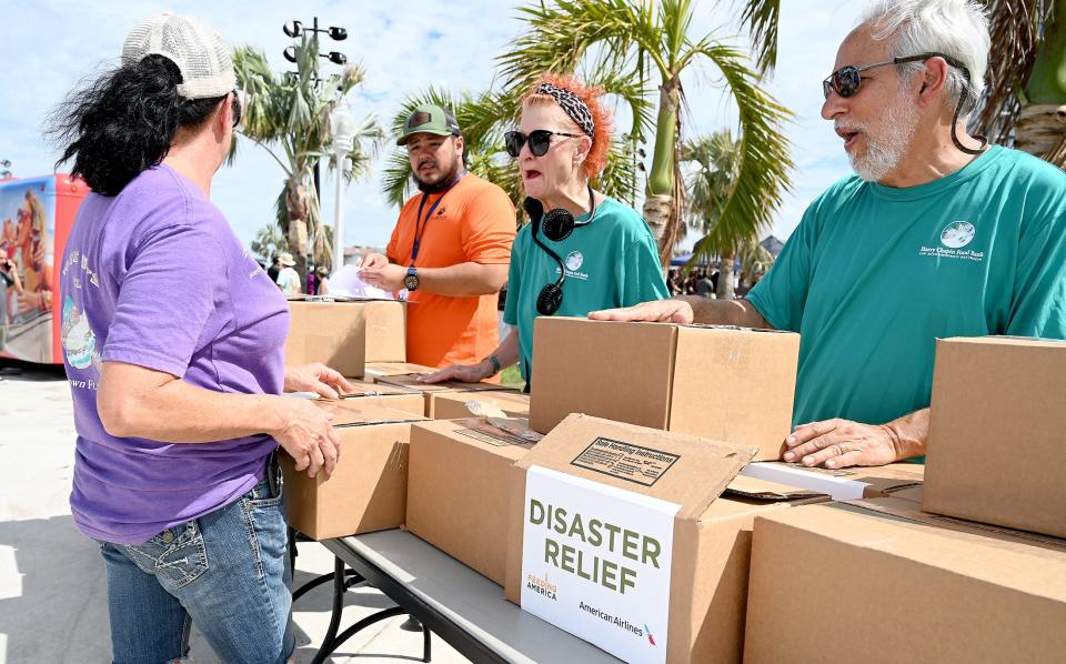 B.J. Santiago, a volunteer with the Harry Chapin Food Bank, distributes disaster relief kits alongside fellow volunteers Joanne and John Gucciardo at the Downtown Community Rally & BBQ at the Caloosa Sound Amphitheater in Fort Myers. The Oct. 12 event offered support in the aftermath of Hurricane Ian.