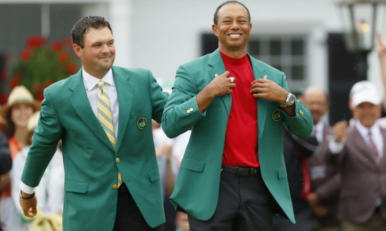 Tiger Woods putting on his green jacket as previous Masters winner Patrick Reed watches.