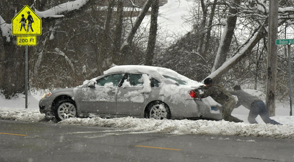 Michael Fuehne, left, and David Fellner Jr., both of Belleville, strain as they push the car of Billy Brownlee out of a pile of snow after Brownlee went sideways while making a turn in Belleville, Ill., on Saturday, Jan. 12, 2019. Multiple deaths on snow-slicked roads were reported in the Midwest as a winter storm swept the region this weekend, snarling traffic in several states and leaving thousands without power. (Tim Vizer/St. Louis Post-Dispatch via AP)