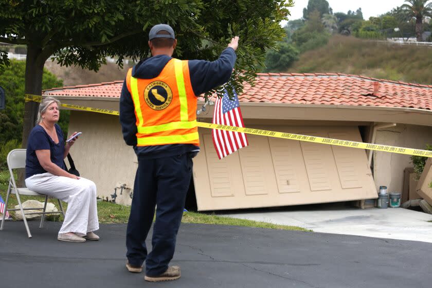 ROLLING HILLS, CA - JULY 9, 2023 -Tim Hong, with California Water Services, talks with a resident who sits in front of her damaged home on Peartree Lane in Rolling Hills Estates on July 9, 2023. Twelve homes were evacuated in Rolling Hills Estates on Saturday night after the ground shifted, causing major cracks and leaving some structures "visibly leaning." The cracks in the homes, which are on Peartree Lane bordering a canyon, were visible on the outside and inside, said Los Angeles County Fire Captain Chiyoshi Hasegawa. Investigators arrived at the scene about 4 p.m. Saturday. (Genaro Molina/Los Angeles Times)