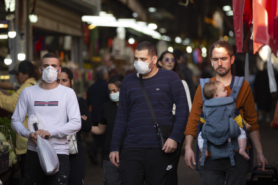 People wear face masks as they shop at a food market in Tel Aviv, Israel, Monday, March 16, 2020. Israel imposed sweeping travel and quarantine measures the government ordered restaurants, malls, cinemas, gyms and daycare centers shut to contain the spread of the coronavirus. For most people, the new coronavirus causes only mild or moderate symptoms. For some it can cause more severe illness. (AP Photo/Oded Balilty)
