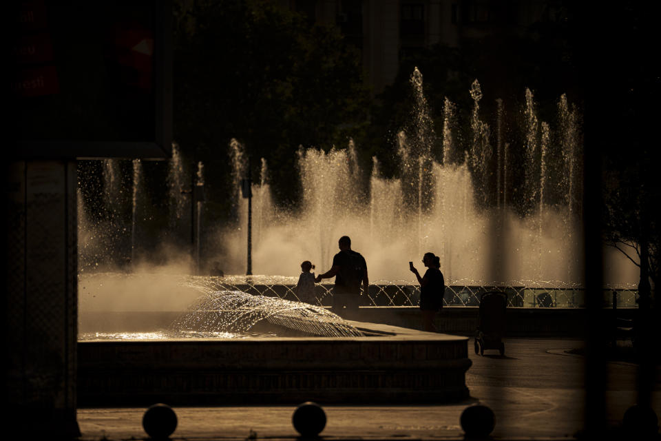 A family walks by a public fountain in Bucharest, Romania, Thursday, July 13, 2023. Weather services issued a heat warning for the current week in southern Romania, with temperatures exceeding 40 degrees Centigrade (104 Fahrenheit) in the shade. (AP Photo/Andreea Alexandru)