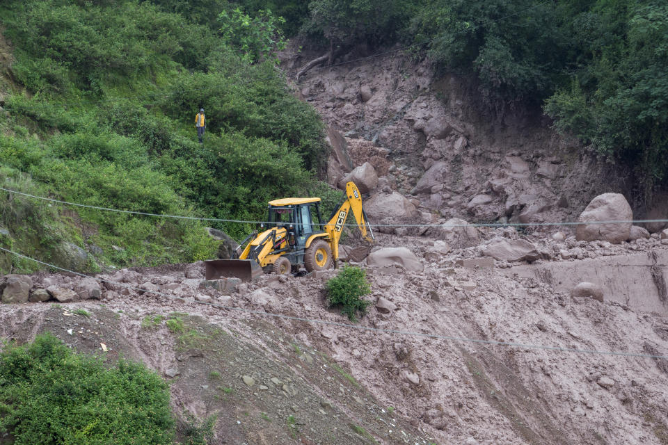 A man stands on a mountain slope and watches an earth-mover being used to remove the debris after a landslide damaged part of a road near Dharamshala, India, Monday, Aug. 14, 2023. Heavy monsoon rains triggered floods and landslides in India's Himalayan region, leaving several people dead and many others trapped. (AP Photo/Ashwini Bhatia)