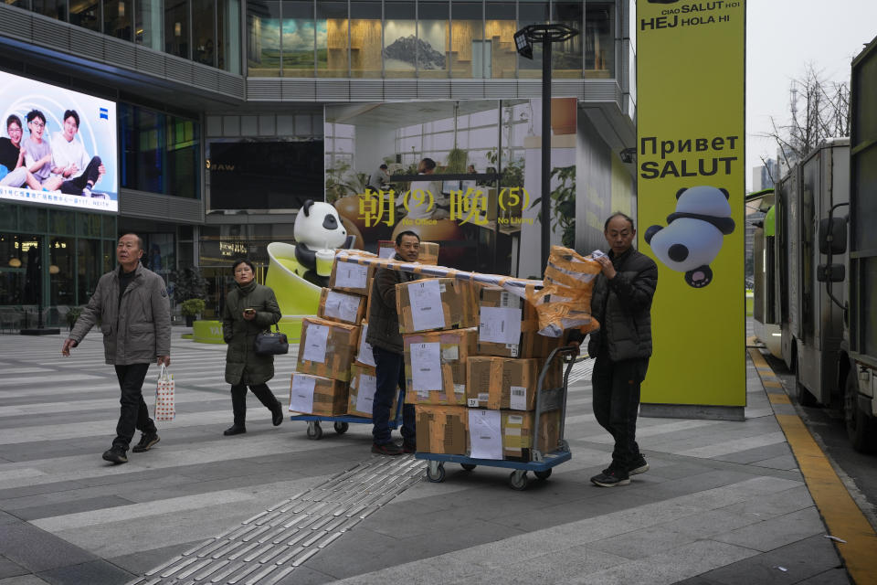 Workers move carts loaded with goods near a billboard promoting office space on a vacant lot at a commercial office building in Chengdu in southwestern China's Sichuan Province on Feb. 27, 2024. China's efforts to restore confidence and rev up the economy will top the agenda during this month’s meeting of the ceremonial national legislature. (AP Photo/Andy Wong)