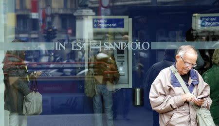 A man stands outside a building as people use Intesa Sanpaolo automated teller machines (ATMs) in Milan October 1, 2013. REUTERS/Stefano Rellandini
