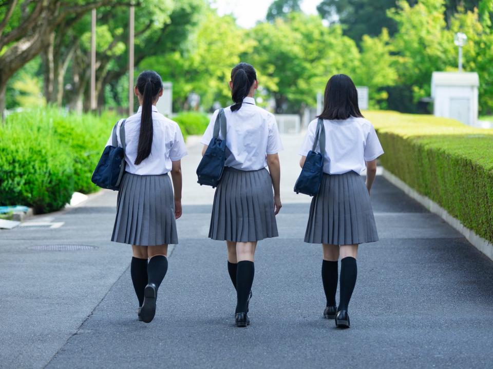 three high school students walking down a road in japan