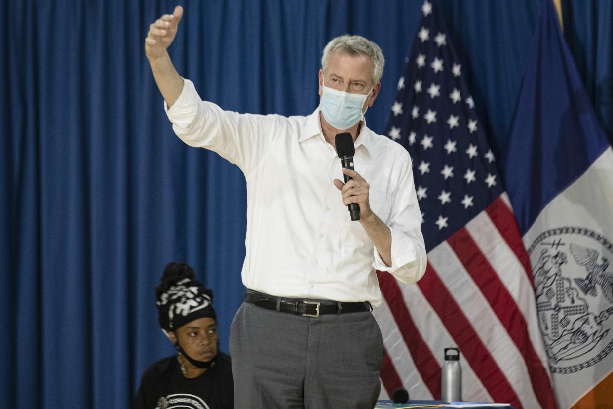 New York City Mayor Bill de Blasio speaks into a microphone through a face mask