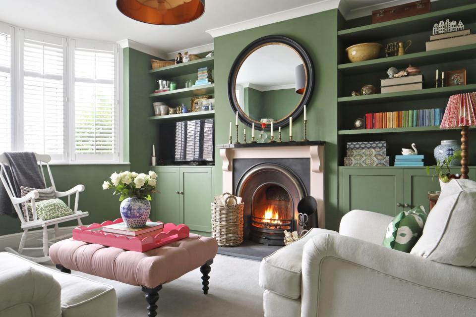 deep green living room with an open fire and in built alcove shelving and sofas in off white