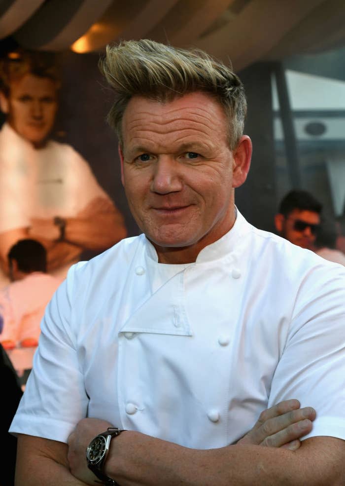 Gordon Ramsay in chef's attire with crossed arms, standing in front of his portrait