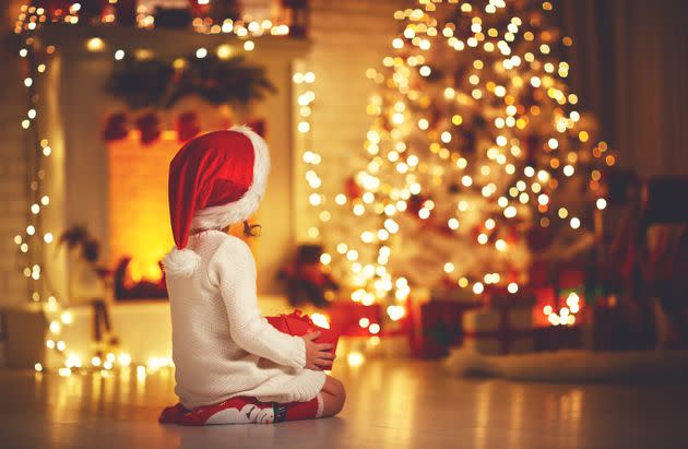 child girl is sitting with her back in front of Christmas tree on Christmas Eve (Photo: evgenyatamanenko via Getty Images/iStockphoto)