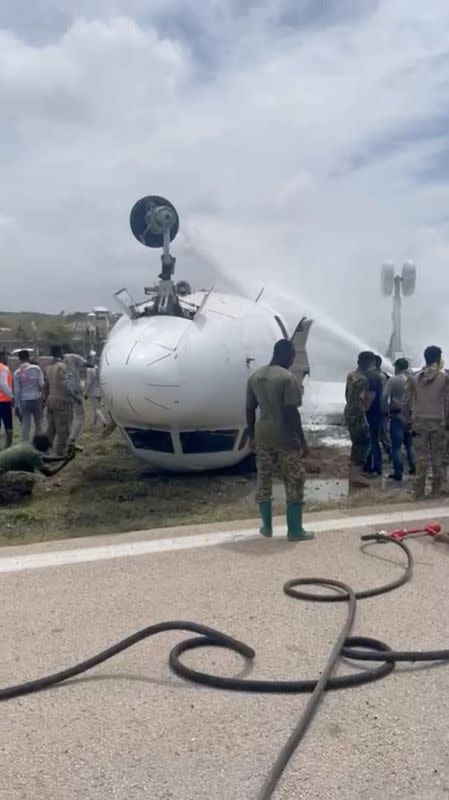 Firefighters spray water on a plane that flipped over after a crash landing, in Mogadishu