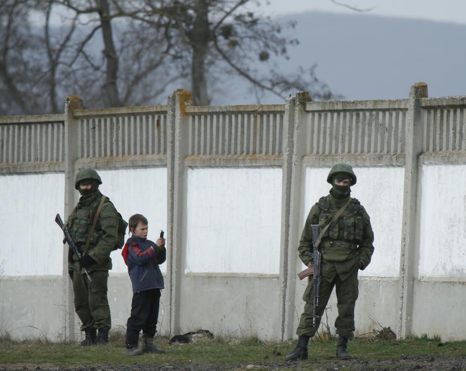 A boy photographs military personnel, believed to be Russian servicemen, standing outside the territory of a Ukrainian military unit in the village of Perevalnoye outside Simferopol