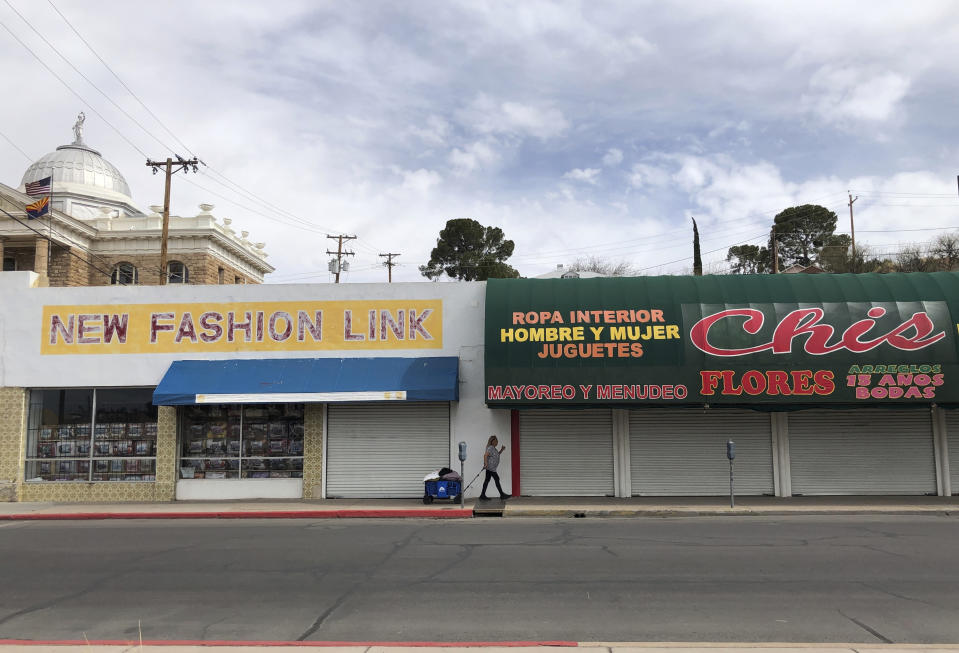 A woman walks past two out-of-business clothing stores located steps away from the U.S.-Mexico border on March 15, 2021 in Nogales, Ariz. The economic wear from nearly 12 months of a partially shut border is easy to spot in downtown Nogales. Bargain clothing stores, money exchanges, secondhand shops and retailers selling plastic knickknacks within walking distance of the border stand closed and many storefronts are boarded up. (AP Photo/Suman Naishadham)