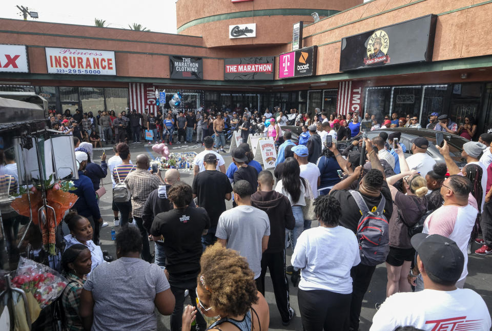 FILE - In this April 1, 2019 file photo, fans of rapper Nipsey Hussle gather at a makeshift memorial in the parking lot of the Marathon Clothing store in Los Angeles, where Hussle was shot and killed the day before. A year after Hussle's death, his popularity and influence are as strong as ever. He won two posthumous Grammys in January, he remains a favorite of his hip-hop peers and his death has reshaped his hometown of Los Angeles in some unexpected ways. (AP Photo/Ringo H.W. Chiu, File)