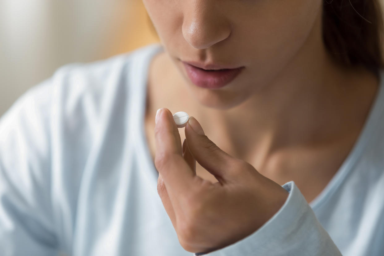 Closeup image of woman face and pill in hand. Sick young female holding white round pill near her mouth and going to take medication as per doctor prescription for recovery. Healthcare medical concept