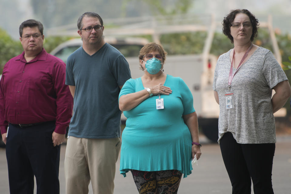 From left, Shasta County Health and Human Services workers Mike Rinehart, Jon Taylor, Melanie Gilchrist and Theresa Ellis stand and watch as the procession for Redding fire inspector Jeremy Stoke passes in Redding, Calif., Thursday, Aug. 2, 2018. Stoke, who died last week in the Carr Fire, was being taken from the coroner's office to a funeral home. Fire officials say a massive blaze in Northern California that has killed six people and torched more than 1,000 homes grew overnight, fueled by wind. The California Department of Forestry and Fire Protection said Thursday firefighters made some gains and the blaze is now a third contained. (AP Photo/Michael Burke)