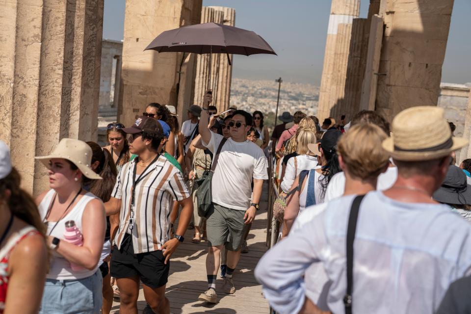 A man holds an umbrella as he and other tourists enters the ancient Acropolis hill during a heat wave, in Athens (AP)