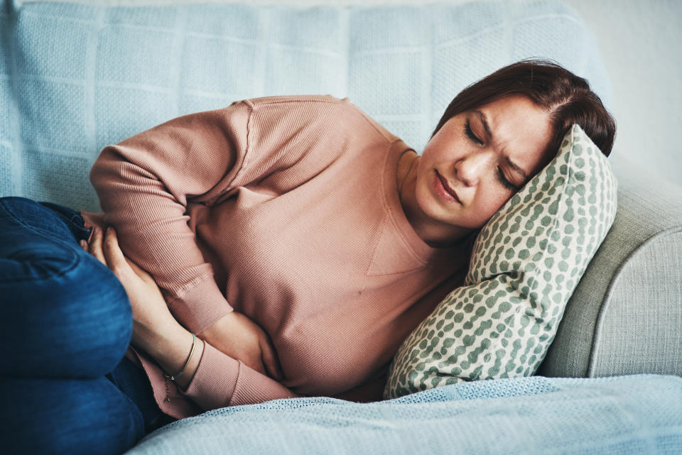 Young woman in pain lying on the couch and holding her stomach