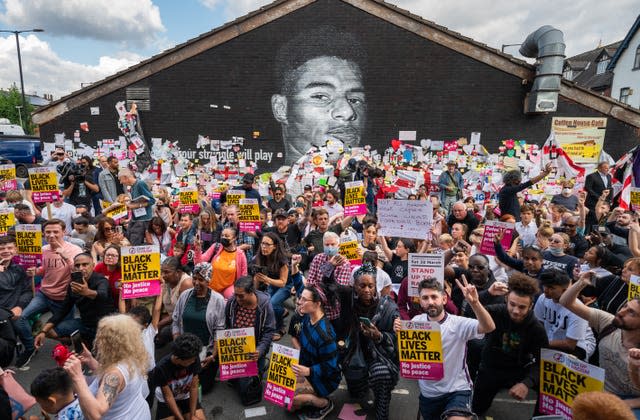 Supporters take the knee during a demonstration in support of England's Marcus Rashford in front of his mural on the wall of the Coffee House Cafe in Withington. The mural appeared to have been vandalised after Rashford missed a penalty in the Three Lions’ Euro 2020 final loss to Italy (Danny Lawson/PA)