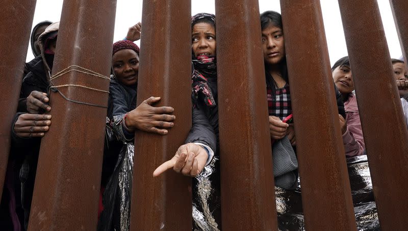 Migrants reach through a border wall for clothing handed out by volunteers, as they wait between two border walls to apply for asylum Friday, May 12, 2023, in San Diego. Hundreds of migrants remain waiting between the two walls, many for days. 