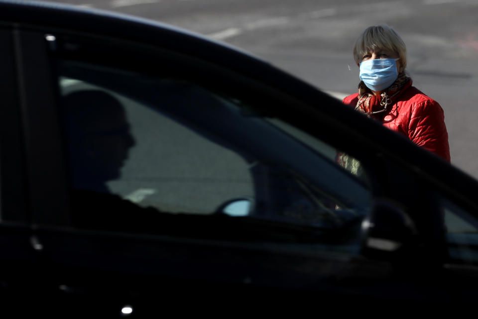 A woman wearing a face mask to protect against the coronavirus, waits to cross a road in London, Tuesday, May 12, 2020, as the country continues in lockdown. Advice from the government is now to wear face covering when entering enclosed spaces such as shops. (AP Photo/Kirsty Wigglesworth)