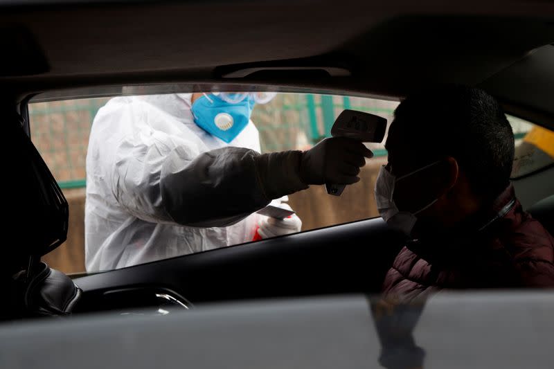 A medical worker in protective suit checks the body temperature of a car passenger at a checkpoint outside the city of Yueyang