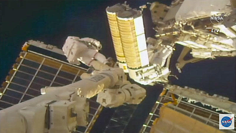 Spacewalker Thomas Pesquet (red stripes on suit) hands a rolled-up solar array (gold cylinders) to Shane Kimbrough before work to install and unfurl the new blankets at the far left end of the International Space Station's power truss. / Credit: NASA TV