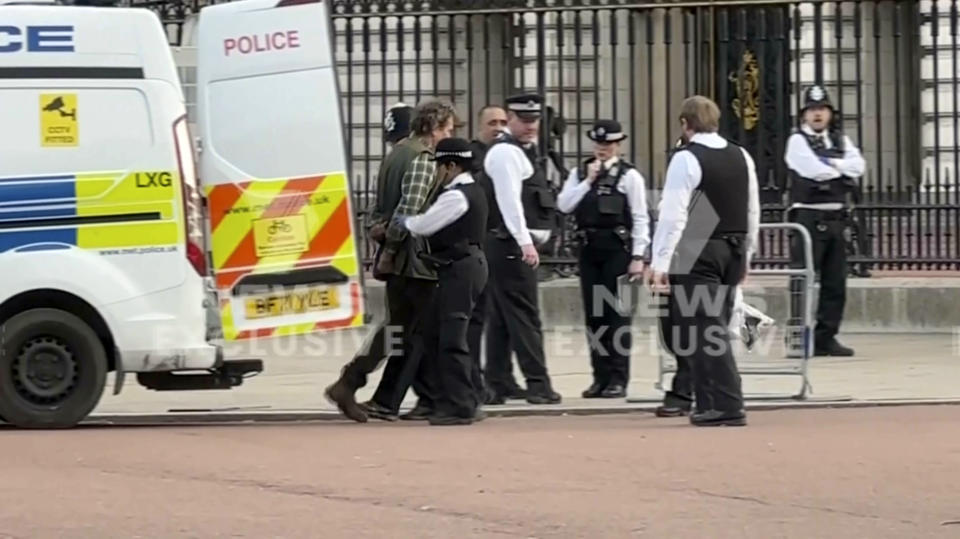 This image from a video shows police leading a man inside a police van outside Buckingham Palace in London, Tuesday, May 2, 2023. London police said a controlled explosion was carried out as a precaution outside Buckingham Palace late Tuesday after a man was arrested there on suspicion of possessing an offensive weapon. (CHANNEL 7 via AP)