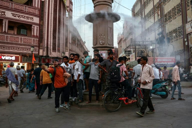 People stand below a water sprinkler installed on a pillar to cool off at a marketplace amid a heatwave in Varanasi, India (Niharika KULKARNI)