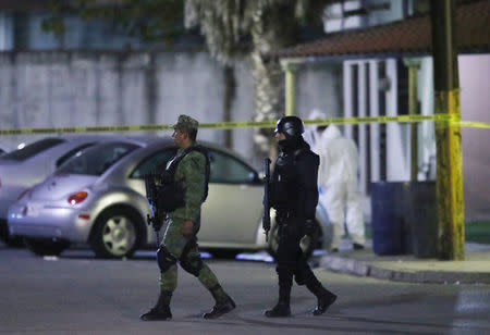 A soldier and a police officer stand guard as a forensic technician works at a crime scene, where men were killed inside a home by unknown assailants, in the municipality of San Nicolas de los Garza, Mexico, January 27, 2018. Picture taken January 27, 2018. REUTERS/Jorge Lopez