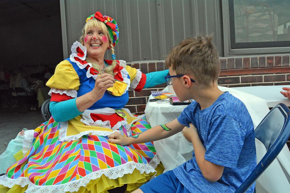 Jackie Newton also known as Sparkie the Clown paints a snake Thursday on the arm of Evan Heuer during the Central Missouri Community Action Bingo for Babies fundraiser in a space at the Arcade District between College Avenue and Fay Street.