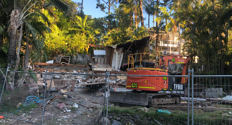 A  red digger demolishing a Gold Coast home on a block of land. 
