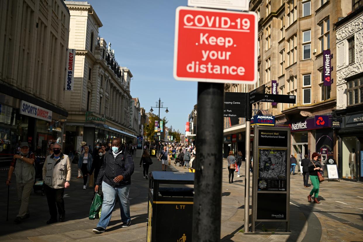 Shoppers, some wearing a face mask or covering, walk past a sign alerting pedestrians to social distance to help mitigate the spread of COVID-19, in Newcastle city centre, north-east England, on September 17, 2020. - The British government on Thursday announced new restrictions for northeast England, the latest region to see a surge in coronavirus cases as Prime Minister Boris Johnson warned of a 