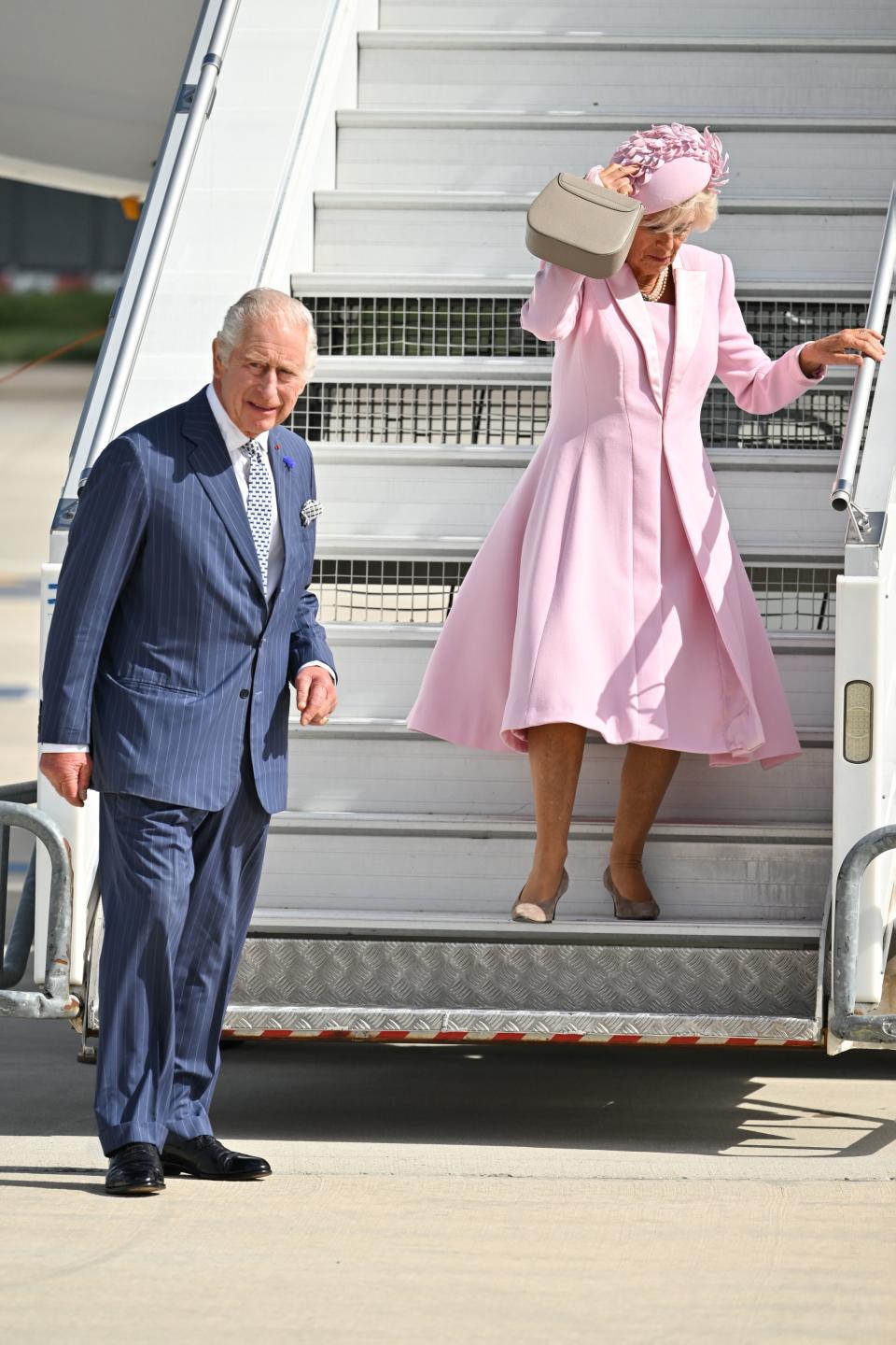 Queen Camilla battled the wind as she clutched onto her hat and skirt as she walked onto the runway (PA)