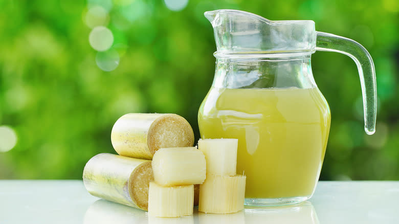 A pitcher of fresh sugar cane juice next to sliced canes