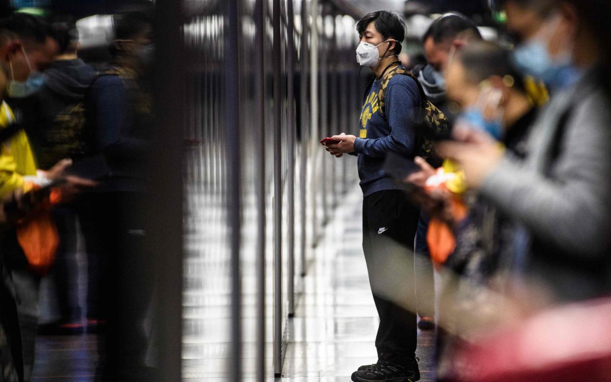 Commuters wear face masks as they wait for a train in Hong Kong's MTR underground metro - AFP