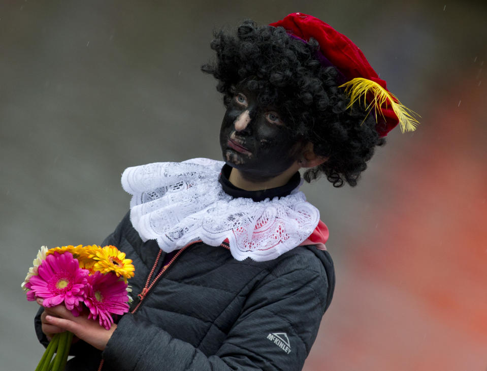 In this Saturday, Nov. 18, 2017, file photo, a child dressed as Black Pete waits for the arrival of Sinterklaas, in Dokkum, northern Netherlands. As many Dutch children eagerly anticipate the arrival of their country's version of Santa Claus this weekend, opponents and supporters of his controversial helper Black Pete are gearing up for protests. Black Pete is often played by white people with their faces daubed in dark makeup. Supporters see him as a traditional children's character, while opponents decry him as a racist stereotype. (AP Photo/Peter Dejong)