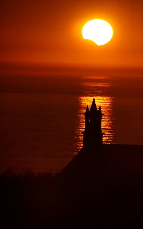 The Saint-They Chapel is seen in silhouette at sunset during a partial solar eclipse as the moon passes in front of the sun seen at the Pointe du Van - Credit: Reuters