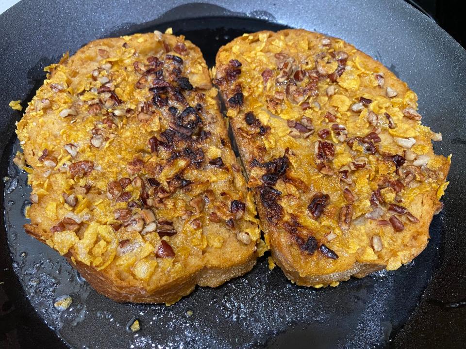 Two pieces of french toast frying in a black pan