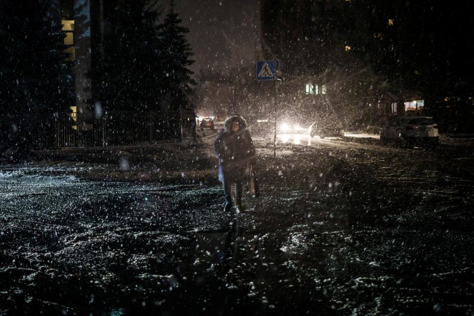 A woman crosses the street during snowfall, as power outages continue in Kyiv (AP)