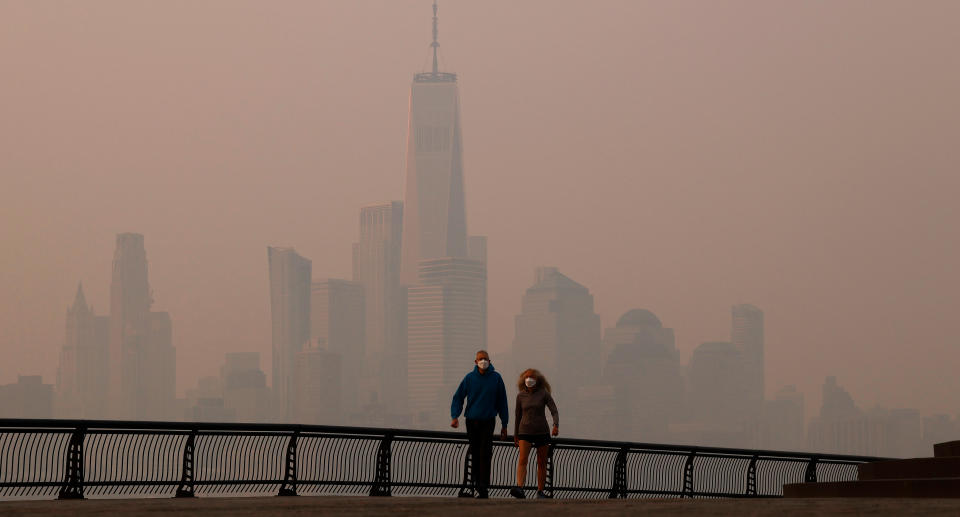 People wearing masks walk along the Hudson River as toxic smog shrouds the skyline of lower Manhattan and One World Trade Center as the sun rises in New York City on June 8, 2023, as seen from Hoboken, New Jersey.  (Photo by Gary Hershorn/Getty Images)