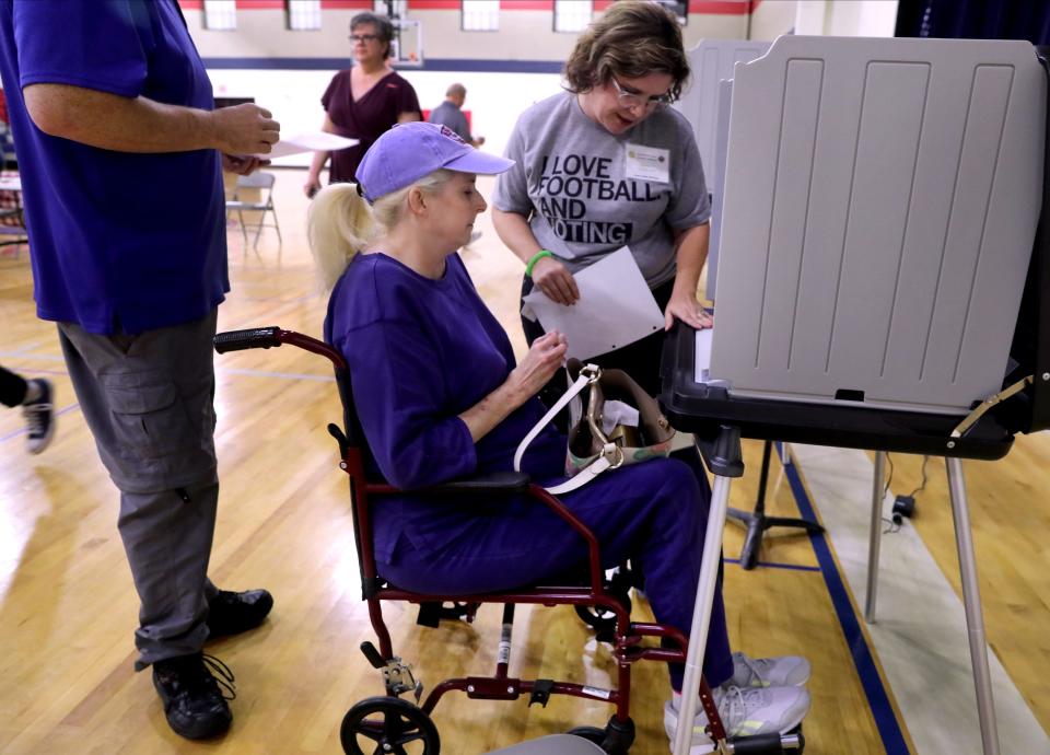 Davina D. Miller-Clements goes over the voting machine with Crissy Sanders as she prepares to vote in the mid-term elections at Hobgood Elementary, on Tuesday, Nov. 8, 2022, while her husband stands behind her wheelchair waiting his turn to vote. 